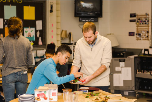 a teacher helps an On the Road Youth in an Emerging Chefs cooking class